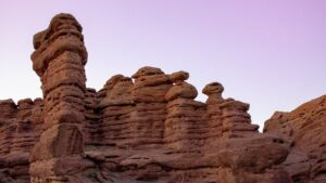 Tall red sandstone rock formations against a pale purple sky.