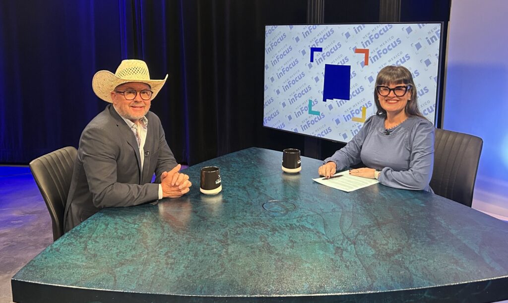 A man in a cowboy hat and a woman in glasses sit across from each other at a desk in a television studio.