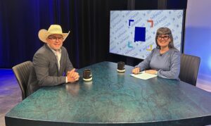 A man in a cowboy hat and a woman in glasses sit across from each other at a desk in a television studio.