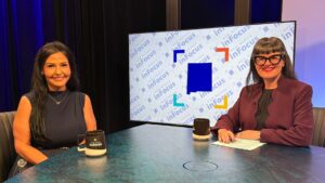Two women sit at a news desk in a studio, with the New Mexico InFocus logo displayed on a large screen behind them.