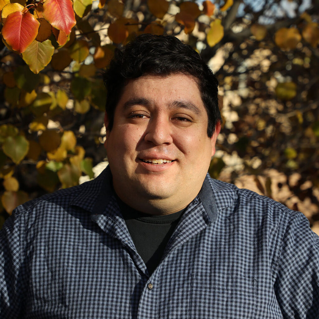 A man smiling in front of a tree.