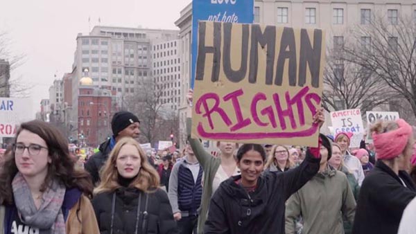 Protestors march, with one holding up a sign reading "HUMAN RIGHTS".