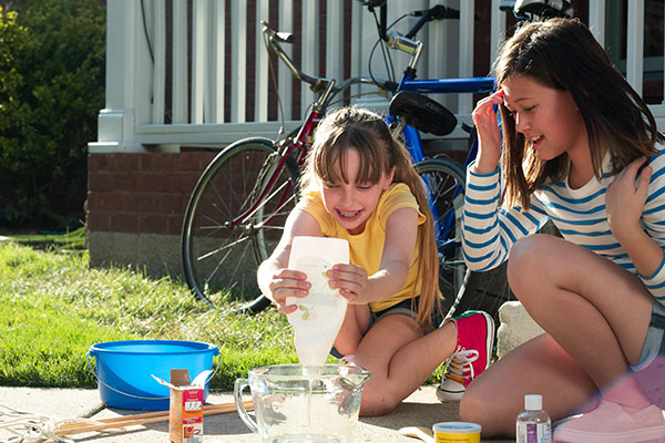 Brand_Image_Still_Bubble-Maker_Two-Girls-Make-Soap-Mix-for-Bubbles_DSCF9022_00000_JPEG_small Two people work with each other to make a concoction in a front yard.