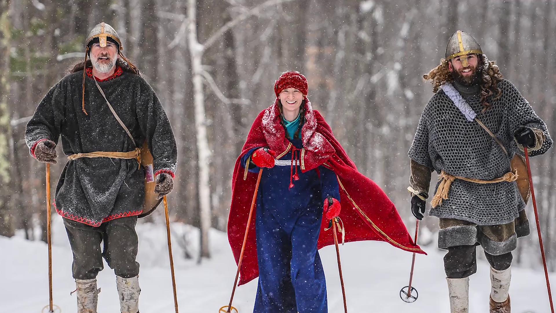 Three people in Nordic dress walk through a snowy forest.