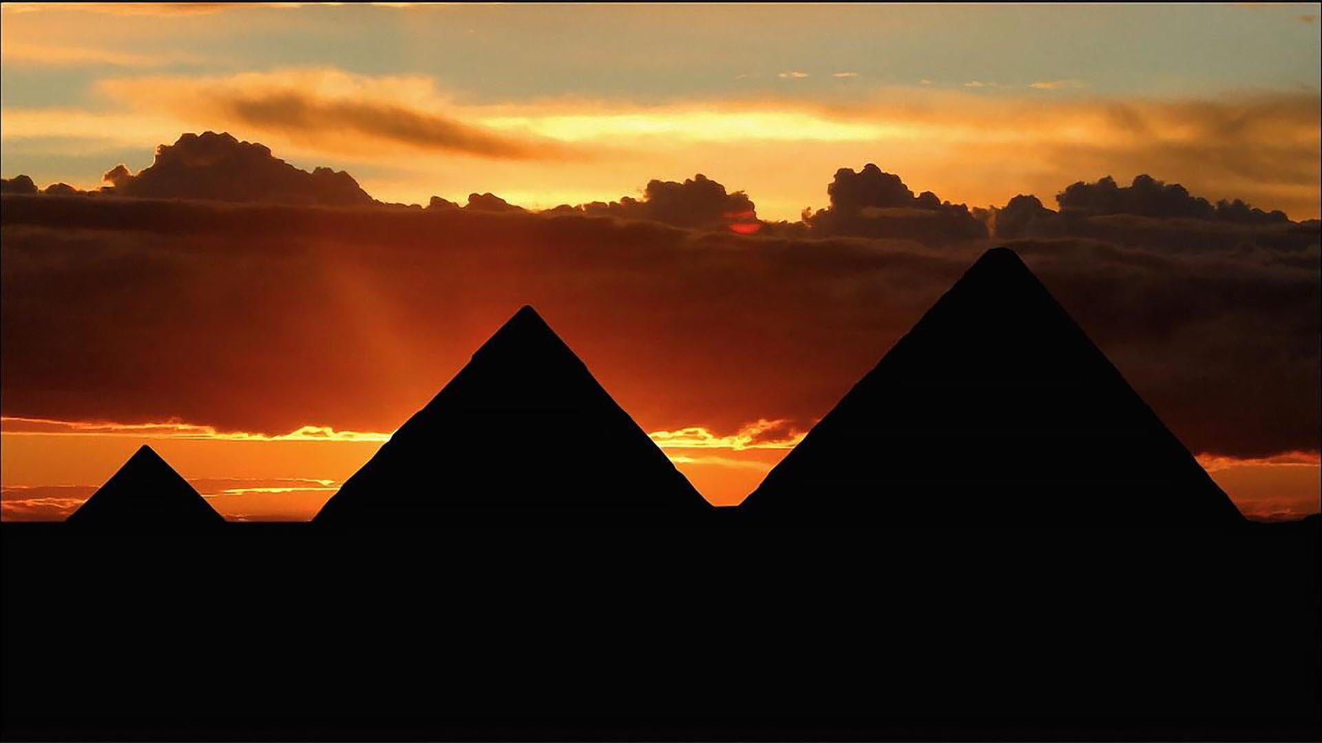Silhouettes of three pyramids at sunset.