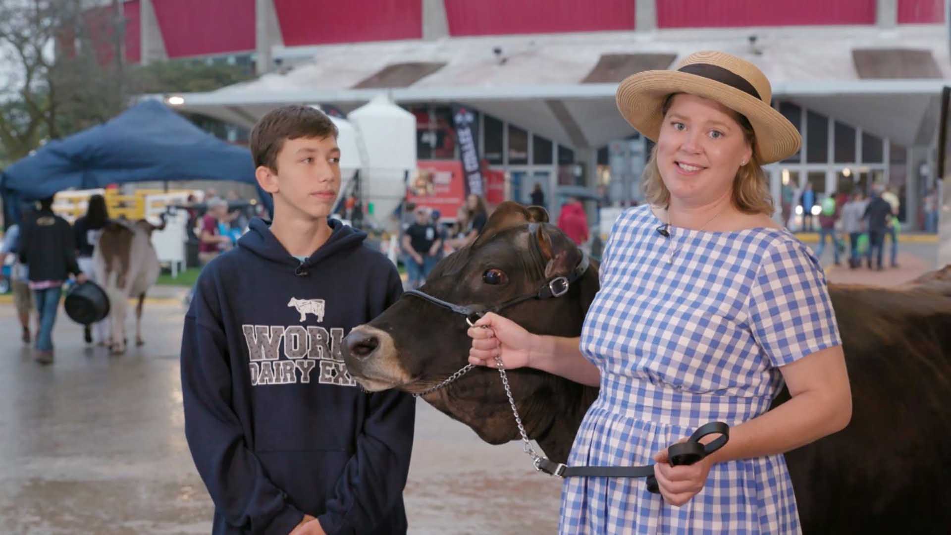A person holds handles for a cow while a teenager looks at them.