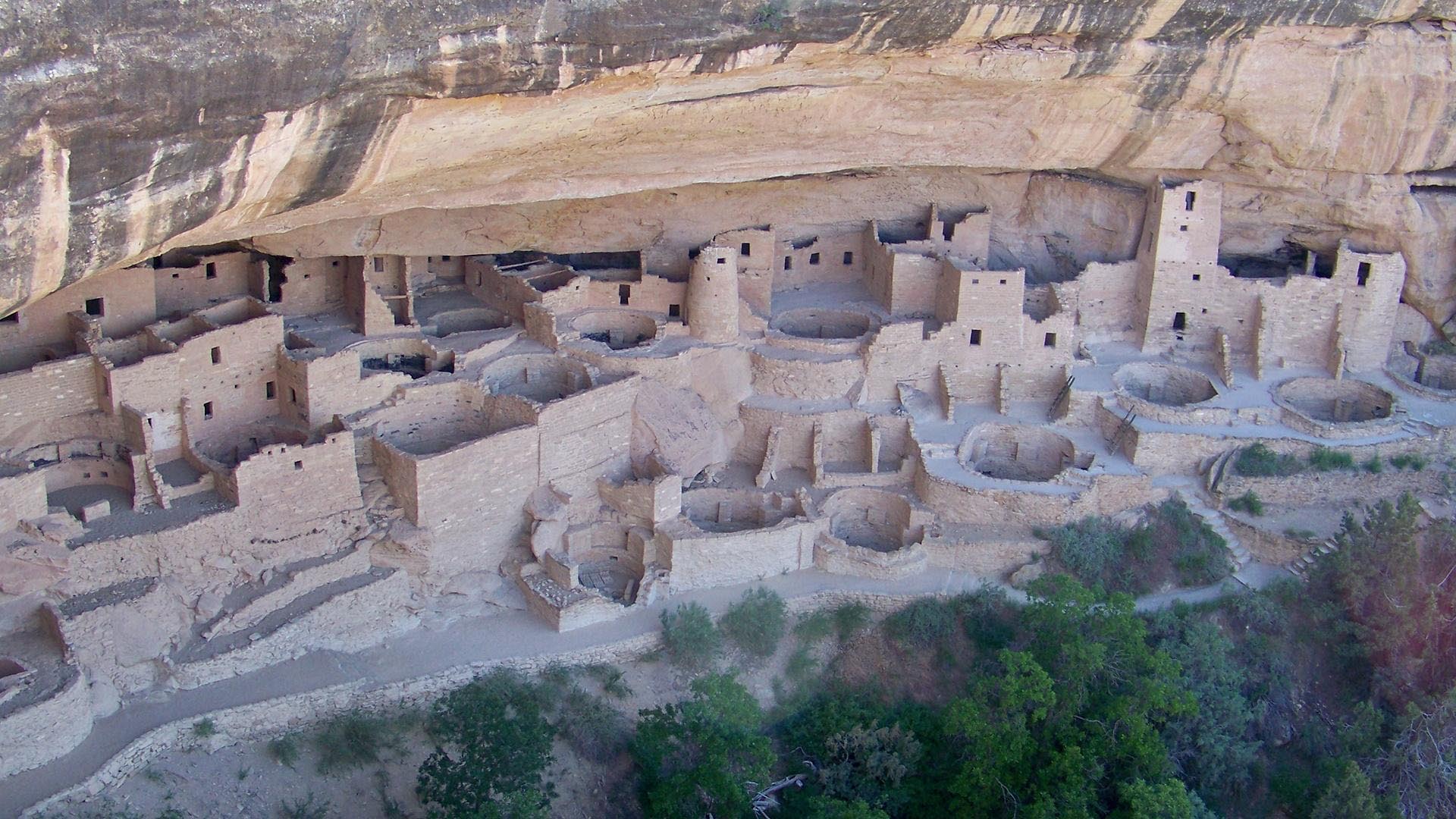 Structures of a Pueblo village next to a cliff.