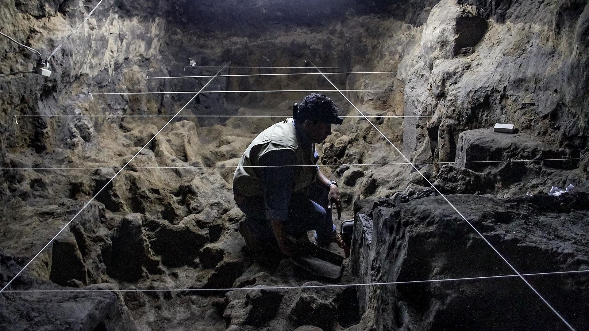 An archaeologist sits and analyzes rocks in a cave.