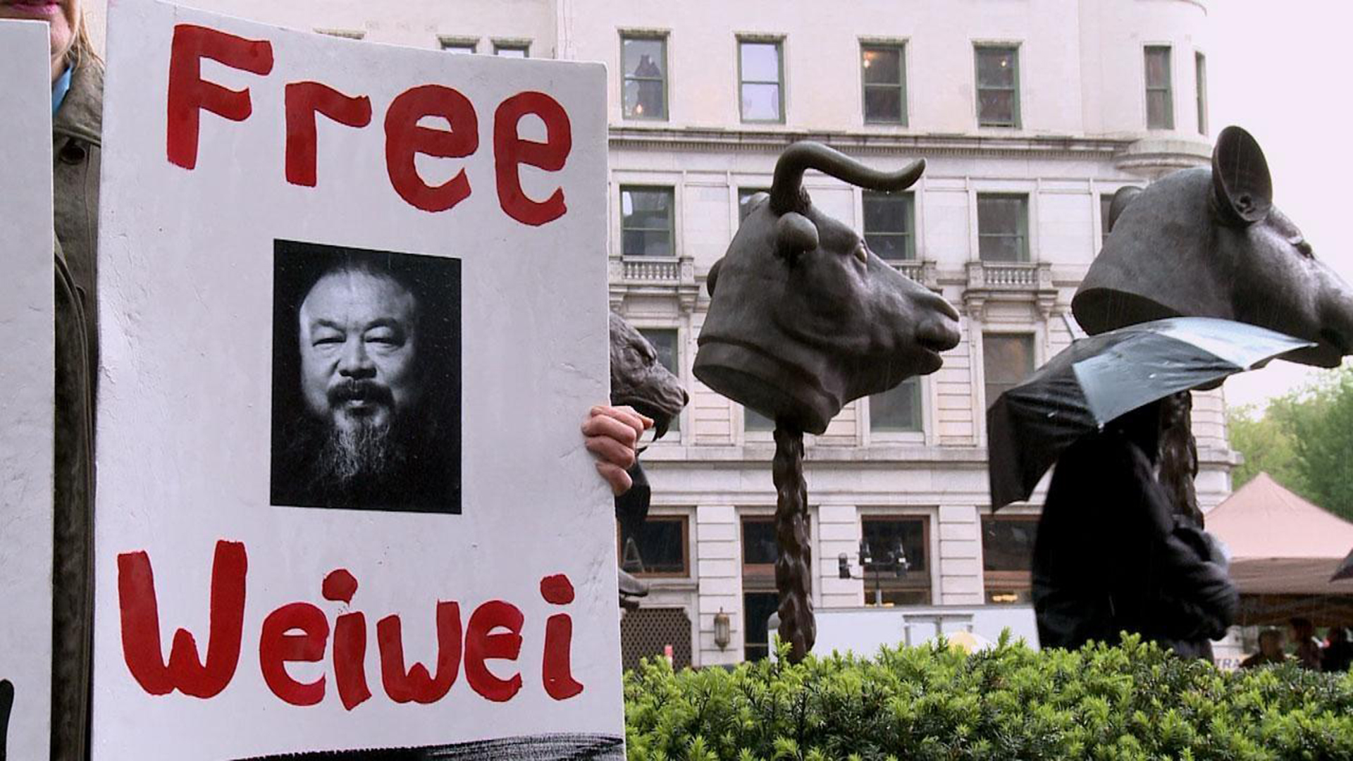 A hand holds up a sign reading "Free Weiwei".