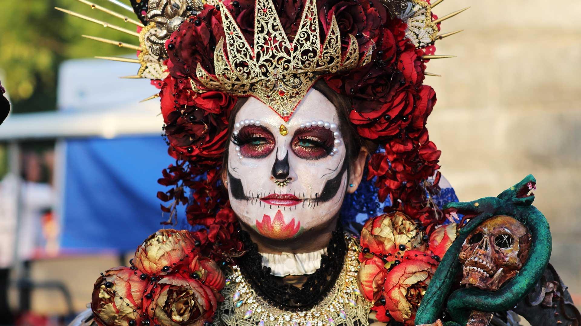 A person in skull makeup and wearing ceremonial regalia.